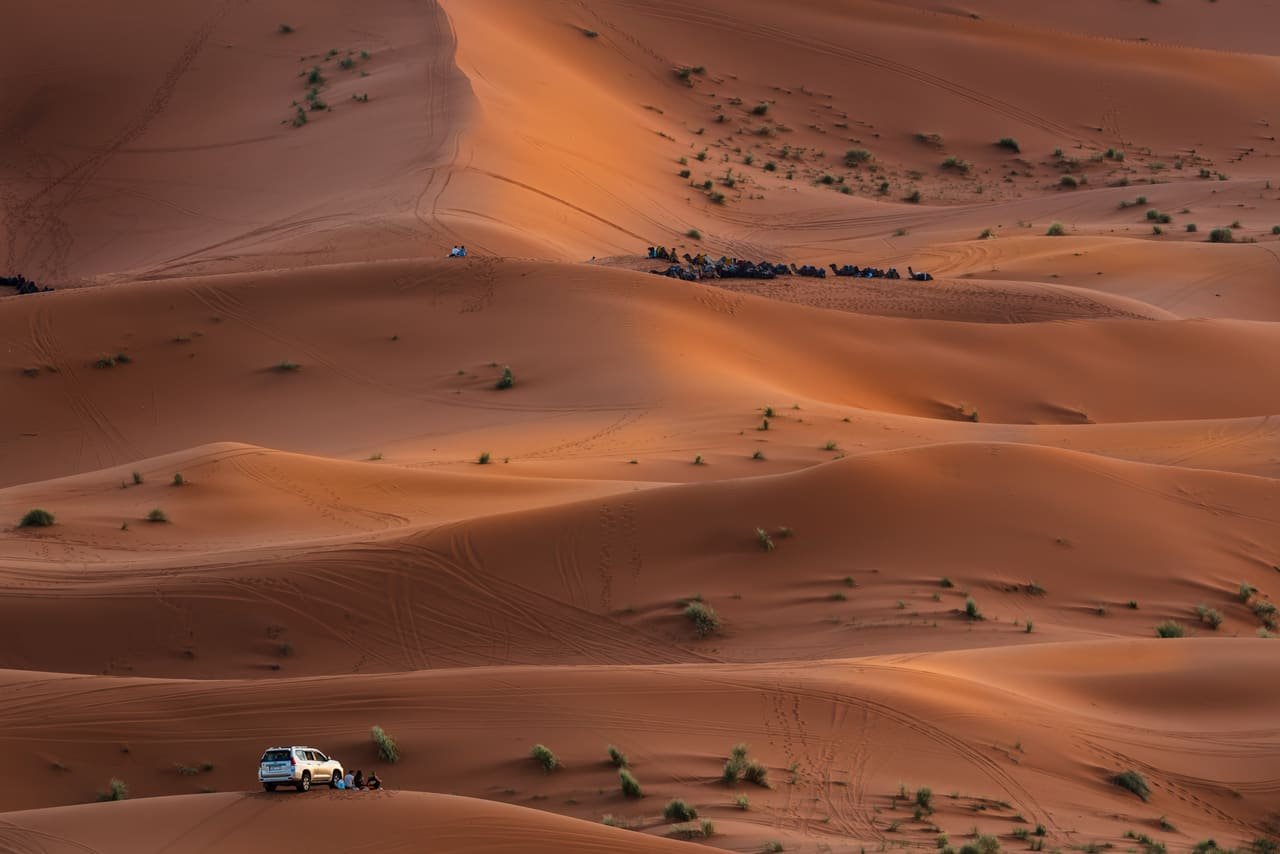 Travellers watching the sun set over the dunes of the Moroccan Sahara